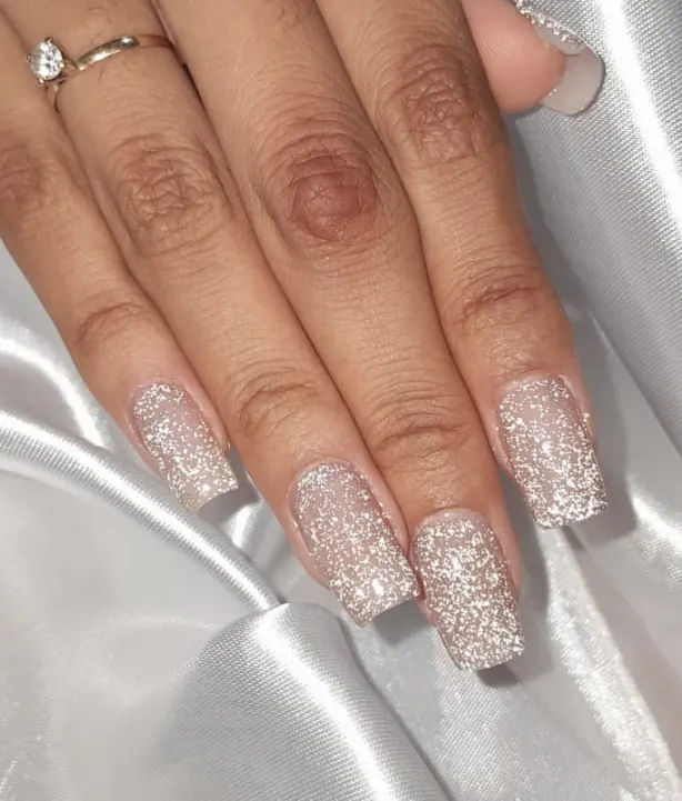 Unhas quadradas com glitter prateado sobre base nude