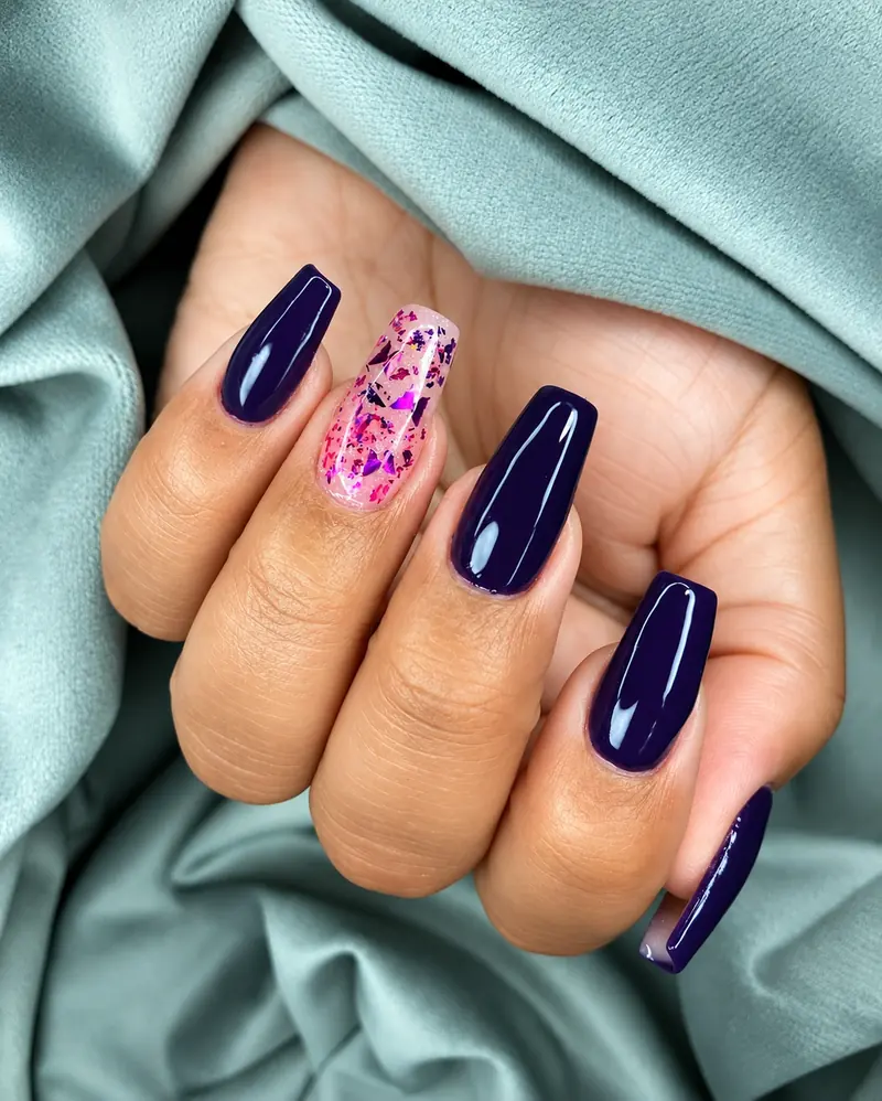 Unhas longas em roxo escuro com uma unha rosa translúcida com flocos